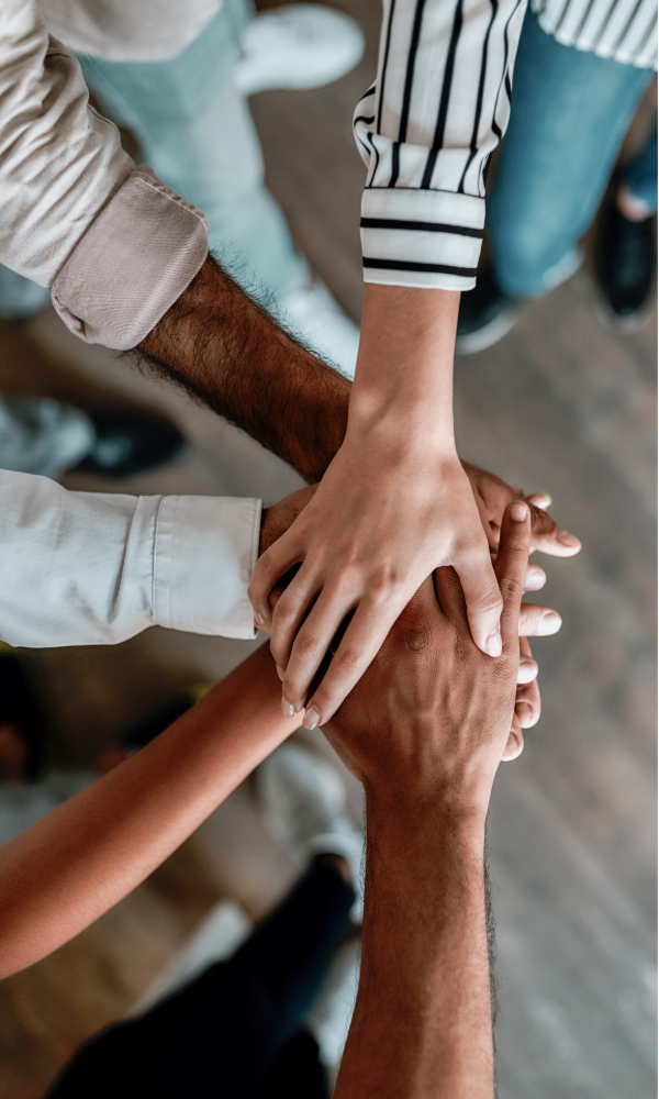 Multiple hands stacked together in a unity gesture, representing human connection and belonging