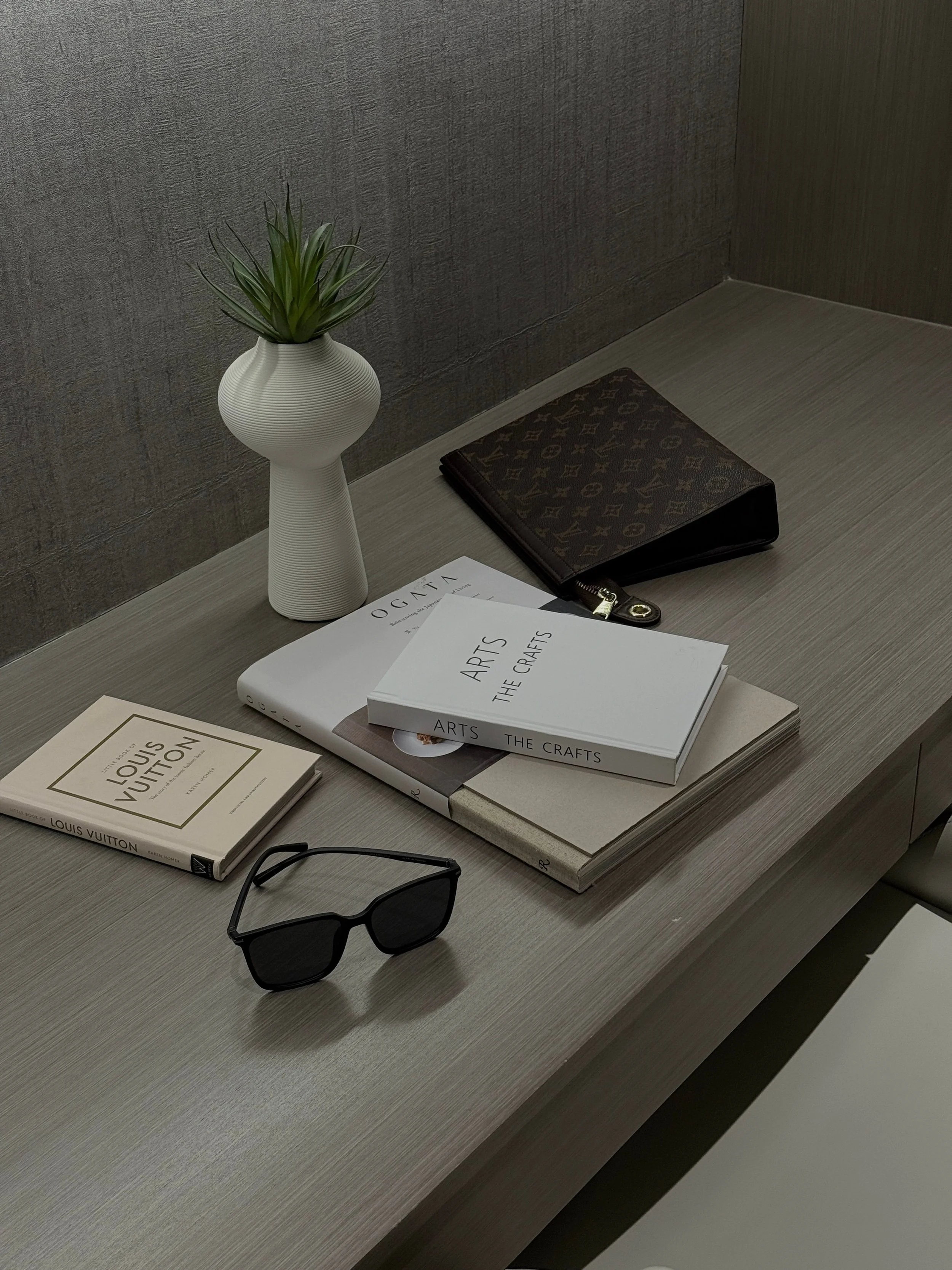 Desk with a potted plant, sunglasses, books, and magazines.
