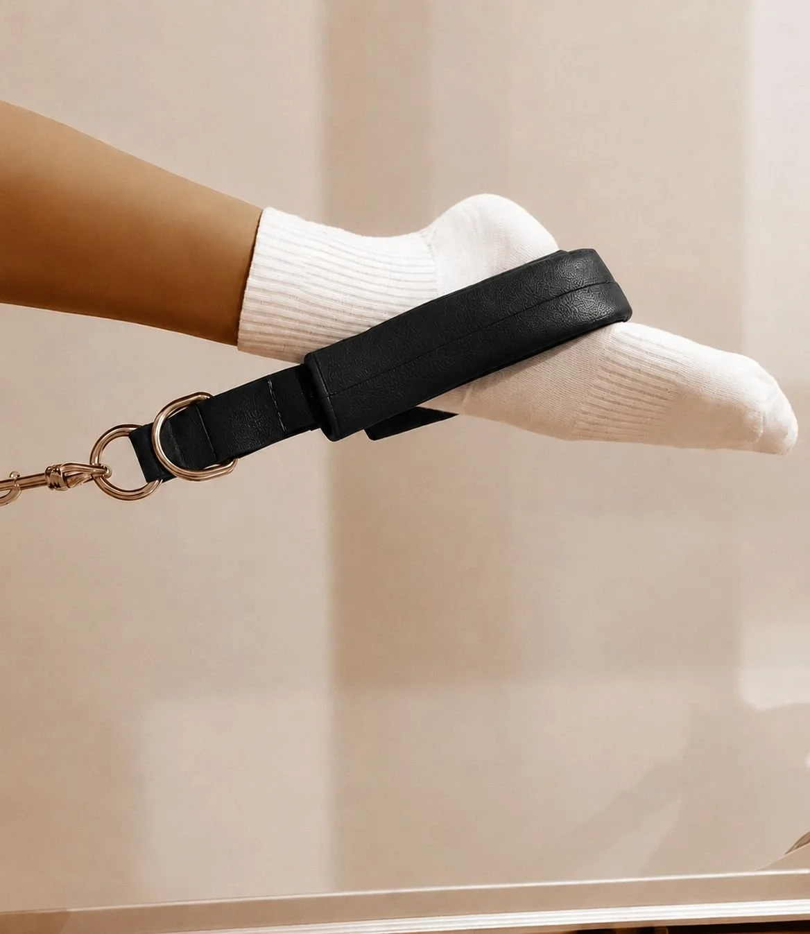 A person wearing a grip sock is using a black leather lagree strap with a gold clip.