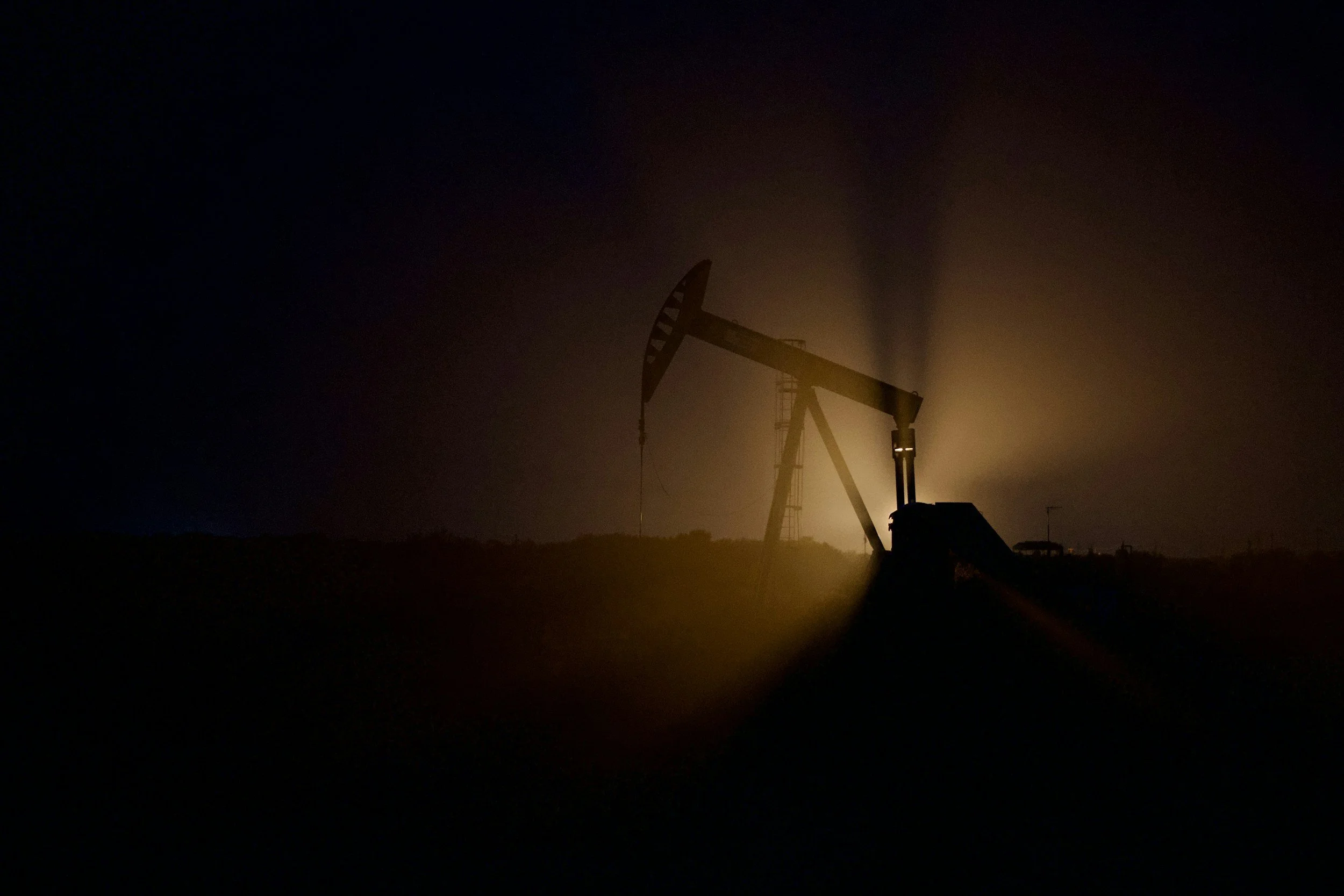 An oil pumpjack silhouetted against a dark night sky with backlighting.