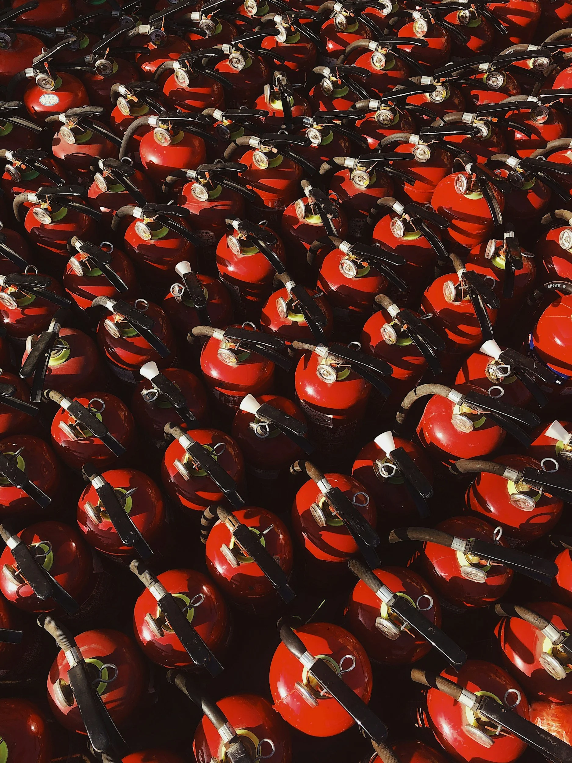 Close-up of multiple red fire extinguishers with black hoses arranged in rows.