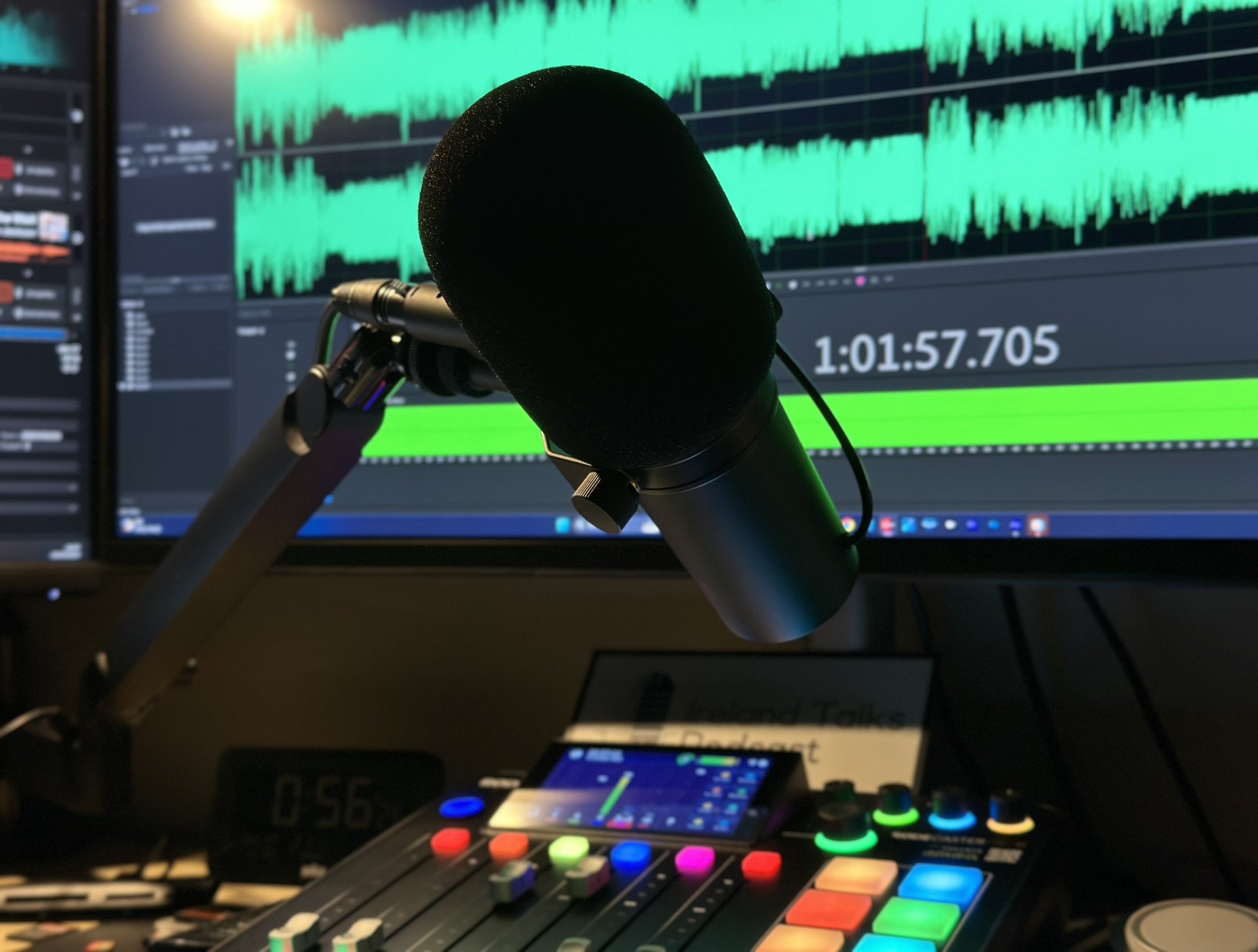 Photo of audio editing equipment with a microphone, soundboard, and a computer monitor showing sound wave graphs.