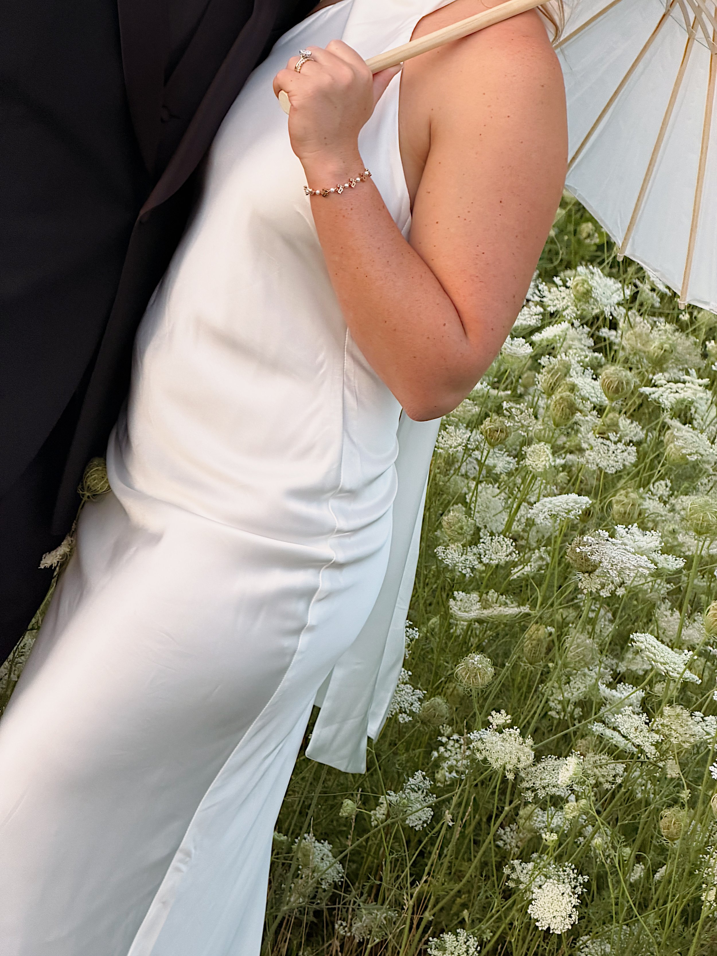 A woman in a white dress holding an umbrella, standing in a field of white flowers.