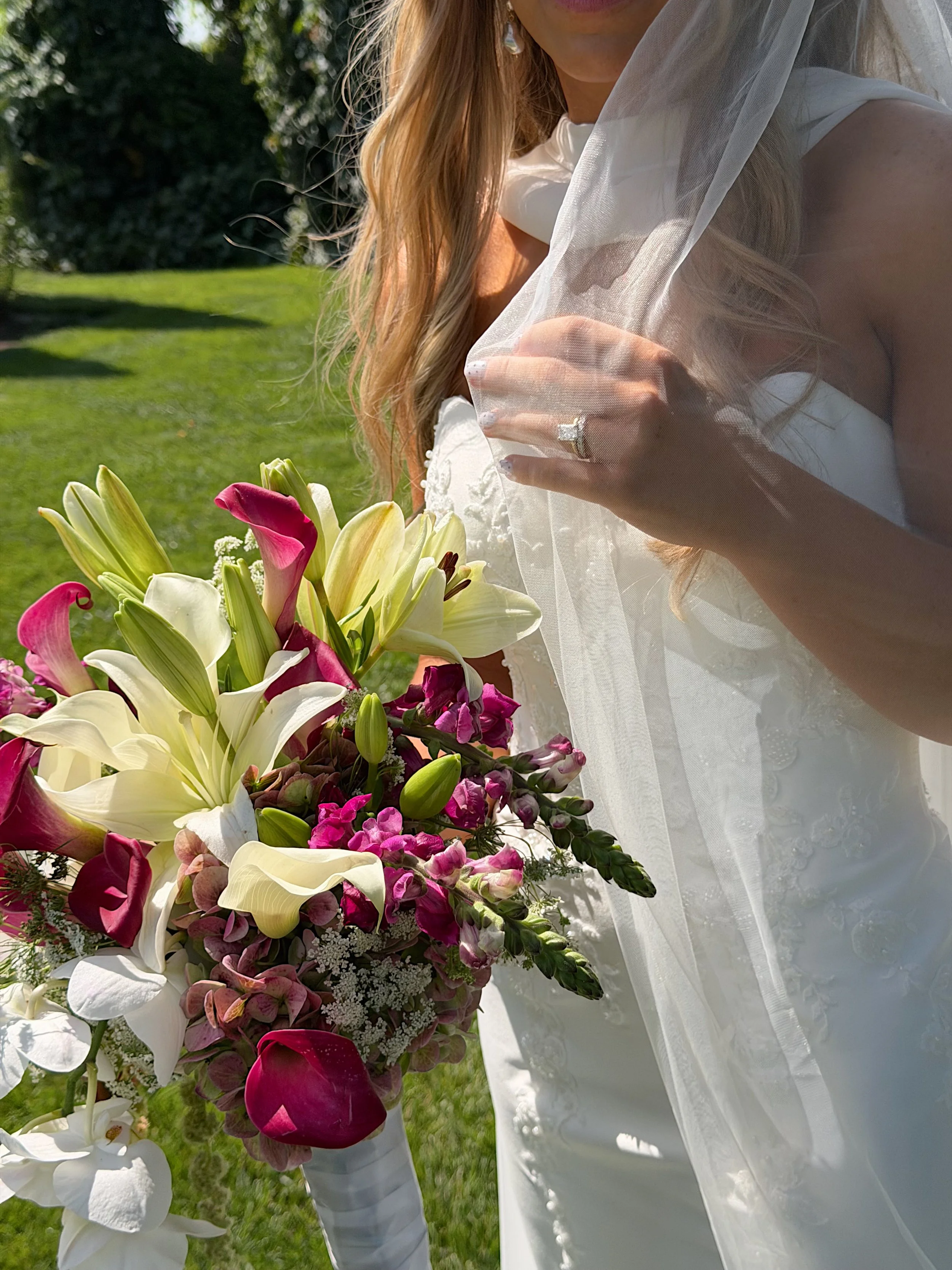 A bride and groom share a kiss at an outdoor wedding venue with rows of chairs, floral arrangements, and a scenic background during sunset.