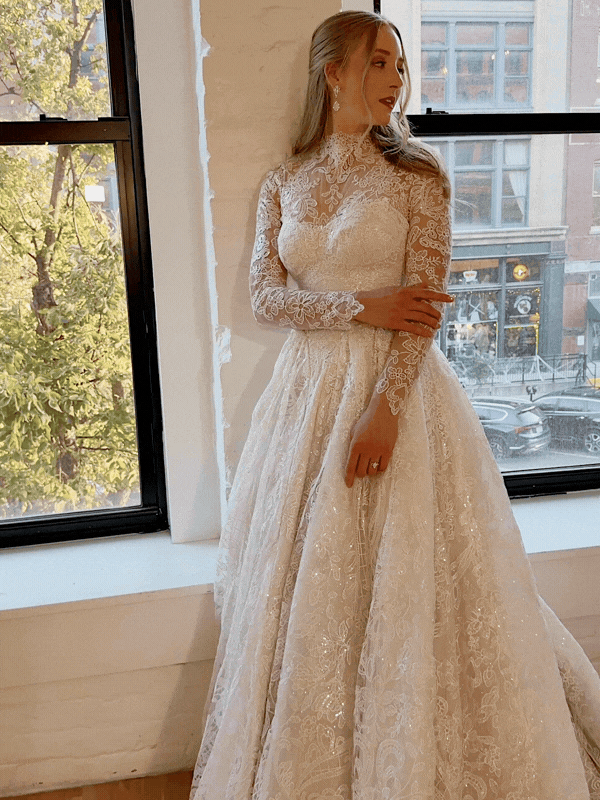 Bride in a white brick downtown room with open windows into the city. Hayley Paige long sleeve dress