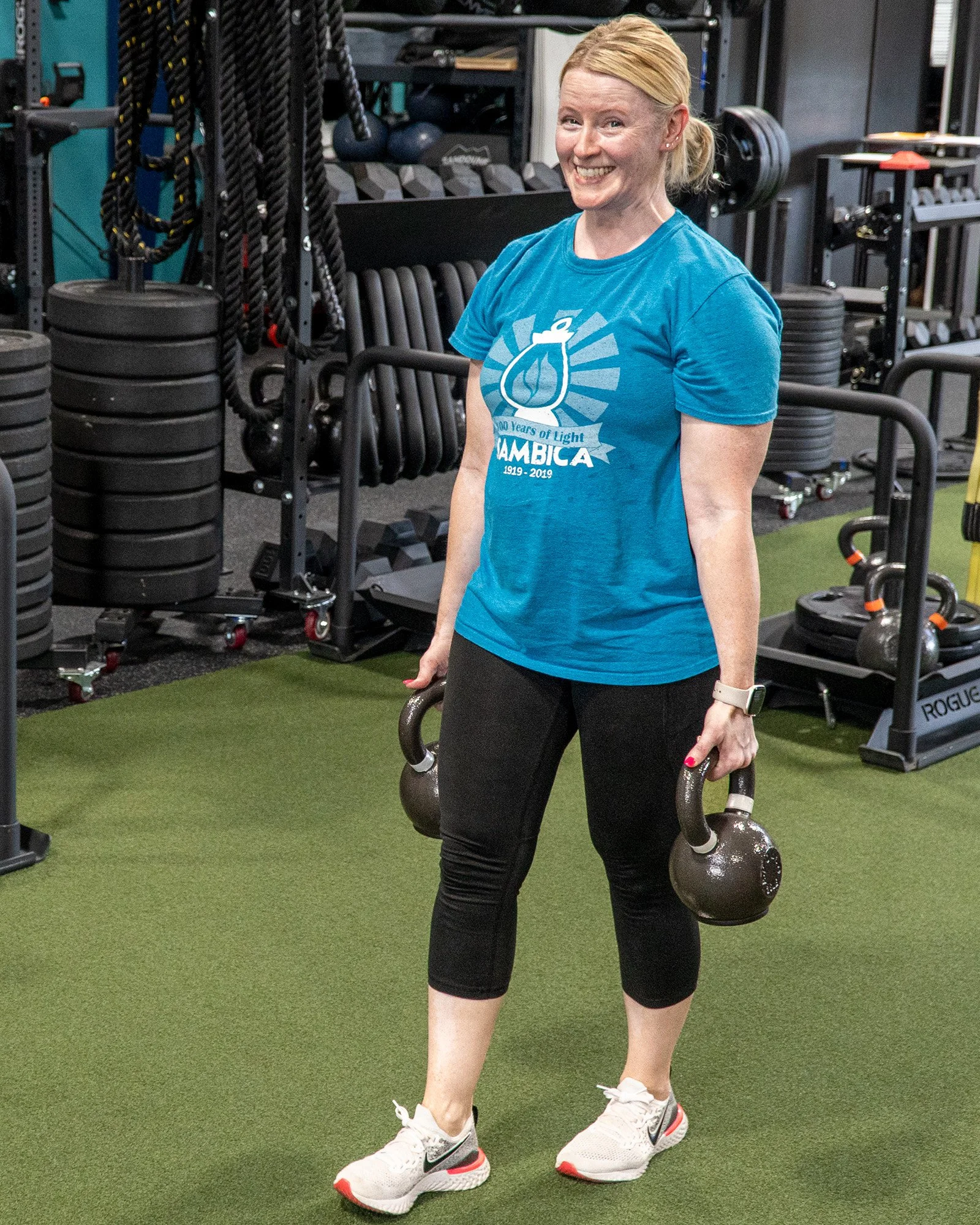 Pink Llama Fitness member smiling with kettlebells during training in Renton