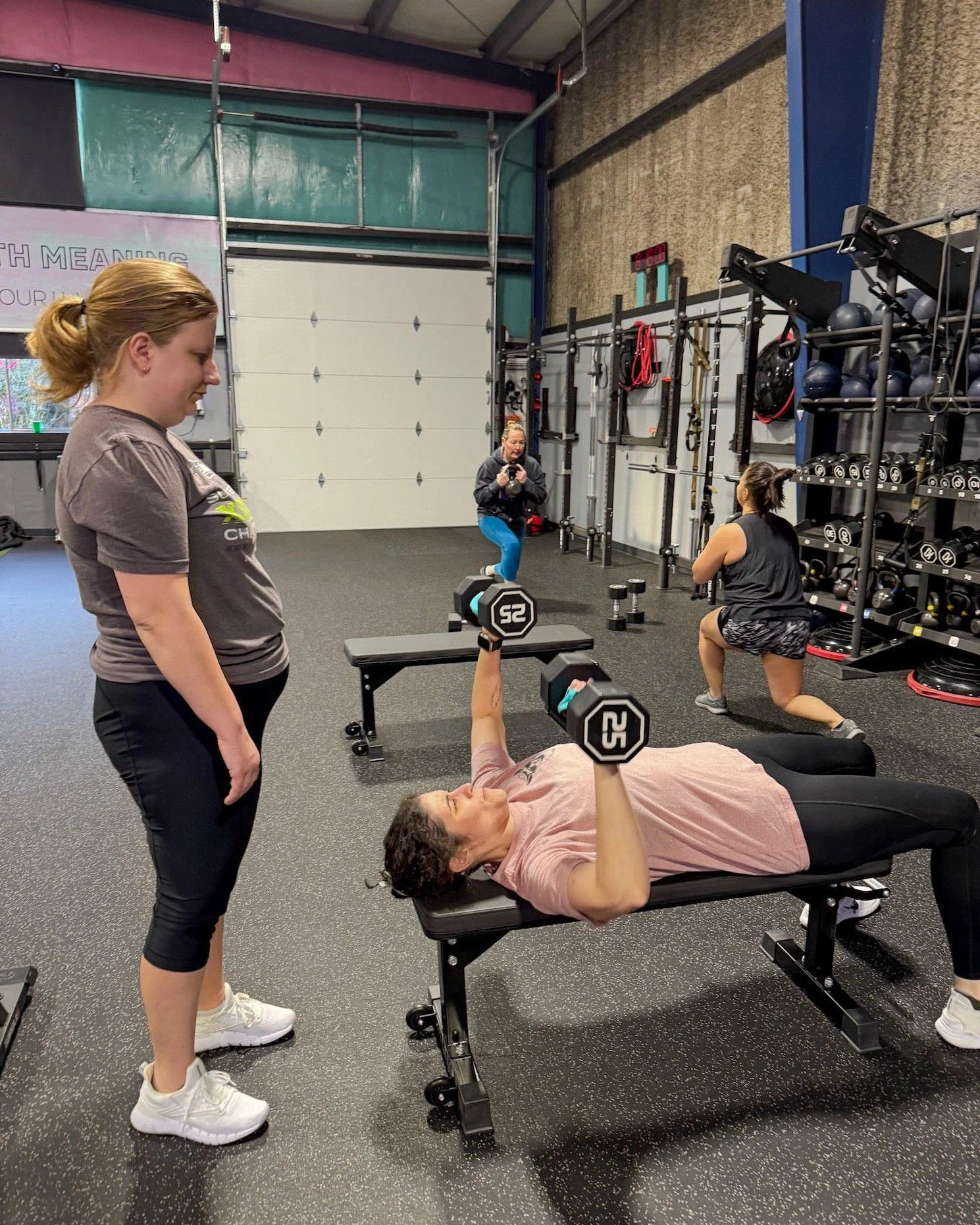 Pink Llama Fitness coach guiding a member through a dumbbell bench press