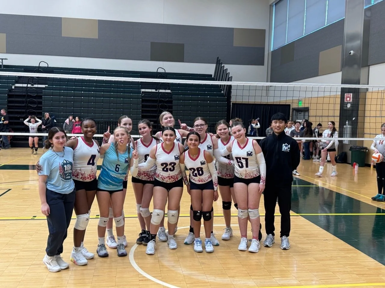 A women's volleyball team in uniform posing with a coach in an indoor gymnasium.