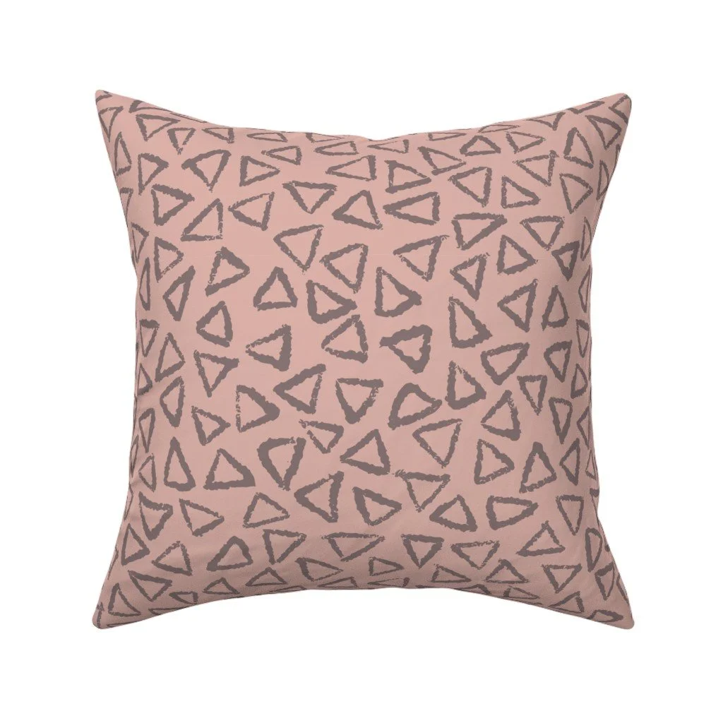 Dusty blush-pink throw pillow patterned with an allover scattered print of textured charcoal-gray outline triangles.