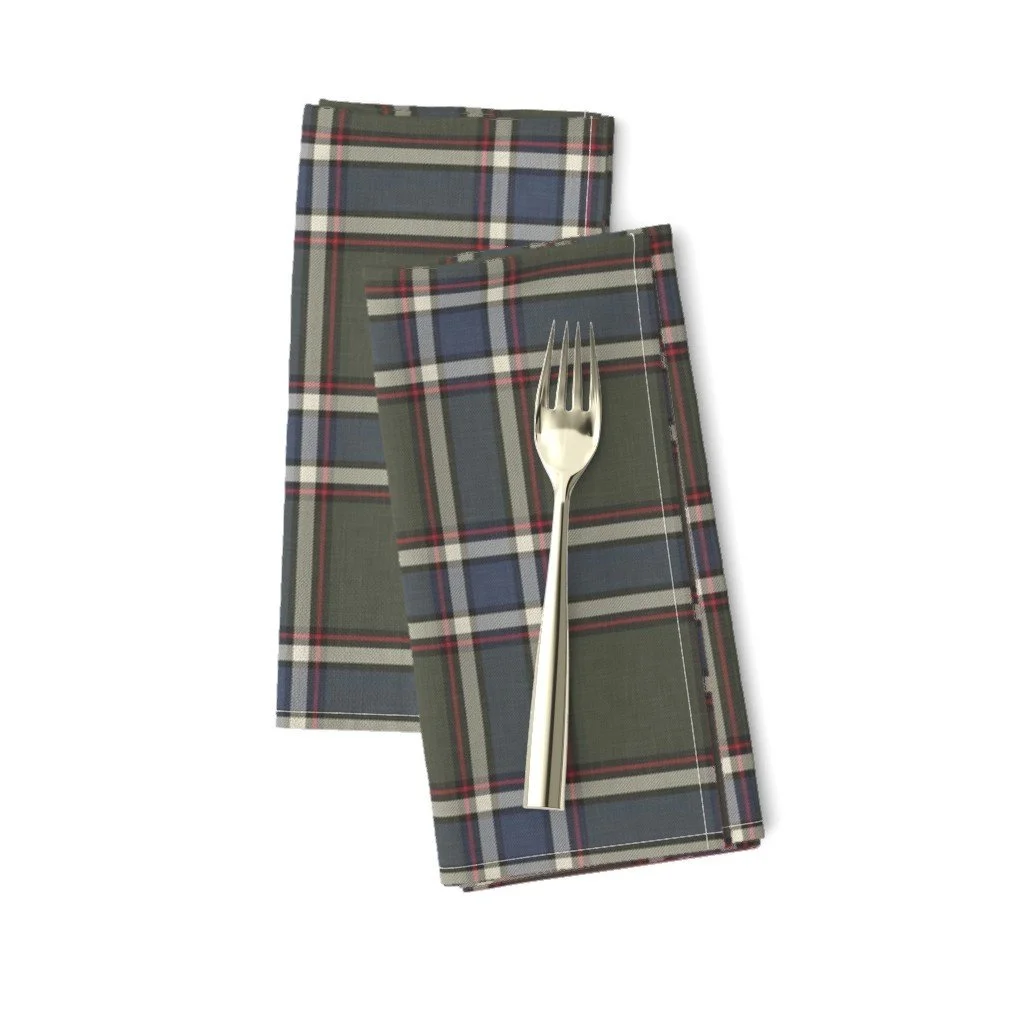 Folded cloth dinner napkins in a dark green and navy plaid with red accent lines, topped with a silver dinner fork.