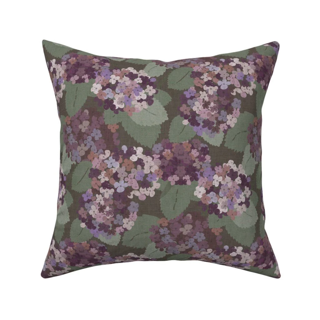 Olive-brown throw pillow patterned with dense, vintage-style hydrangea flower heads in shades of lilac, purple, and dusty rose among green leaves.