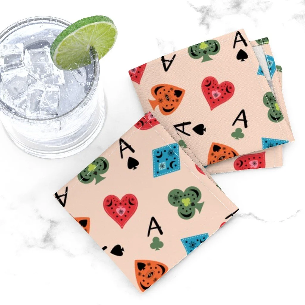 A glass of iced water with a lime wheel on white marble next to blush-pink cocktail napkins printed with mystical playing card suit symbols and aces. 19102124.jpg