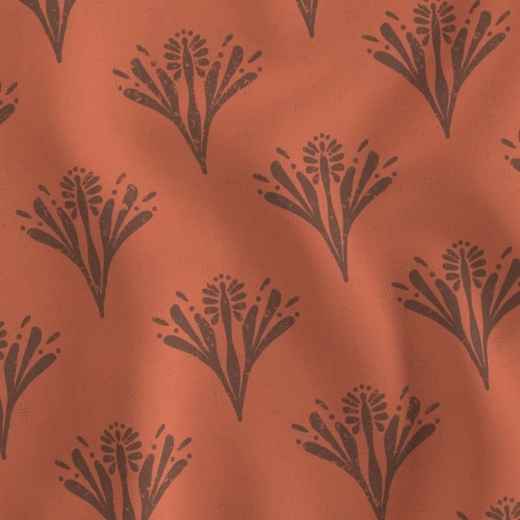 Rust-orange fabric with a repeating block-printed motif of stylized, fan-like dark brown floral sprigs.
