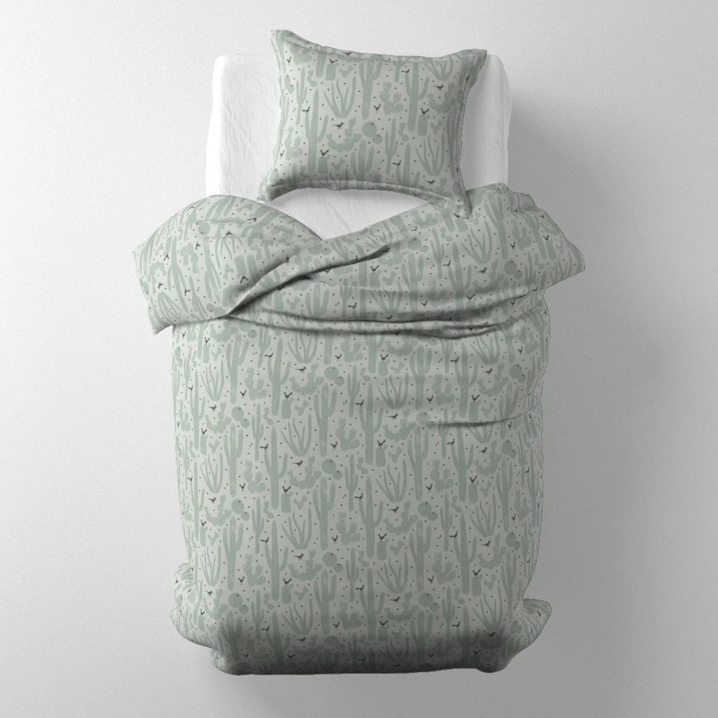 : Bedding set mockup on a single bed featuring pale sage-green duvet and pillow covers printed with desert cacti and small quail.