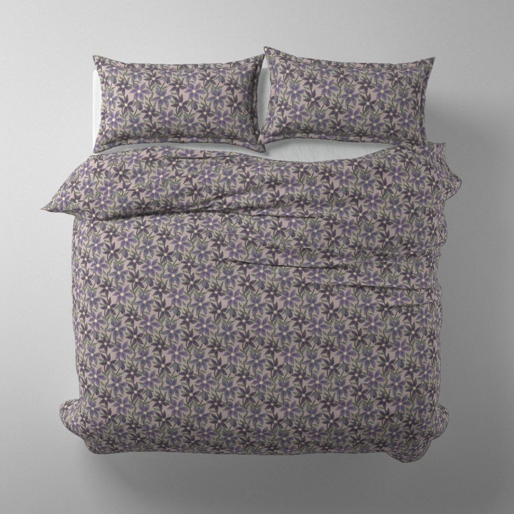 Overhead mockup of a double bed featuring a dusty lavender duvet cover and matching pillowcases with an allover pattern of purple star-shaped flowers and foliage.