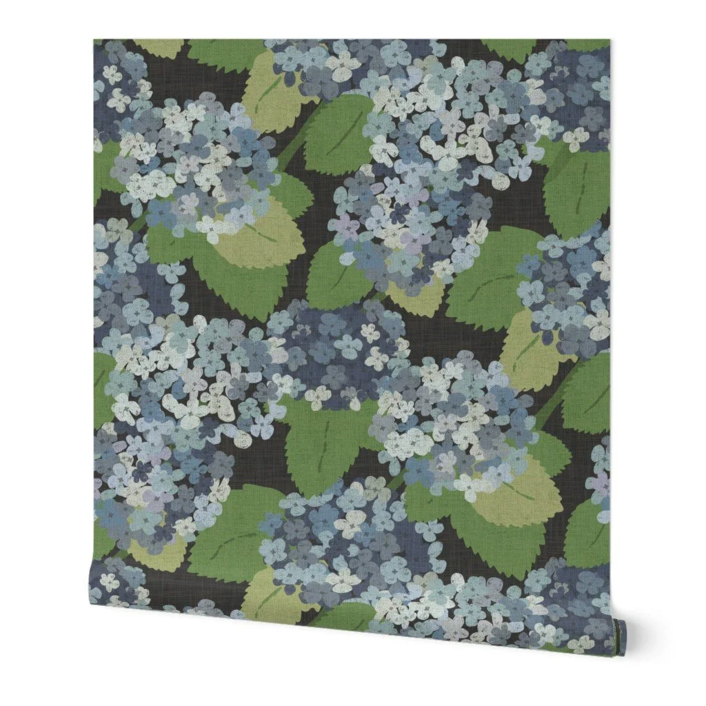 Wallpaper roll with a dark charcoal background showcasing large clusters of blue and periwinkle hydrangea blossoms with textured olive-green leaves.