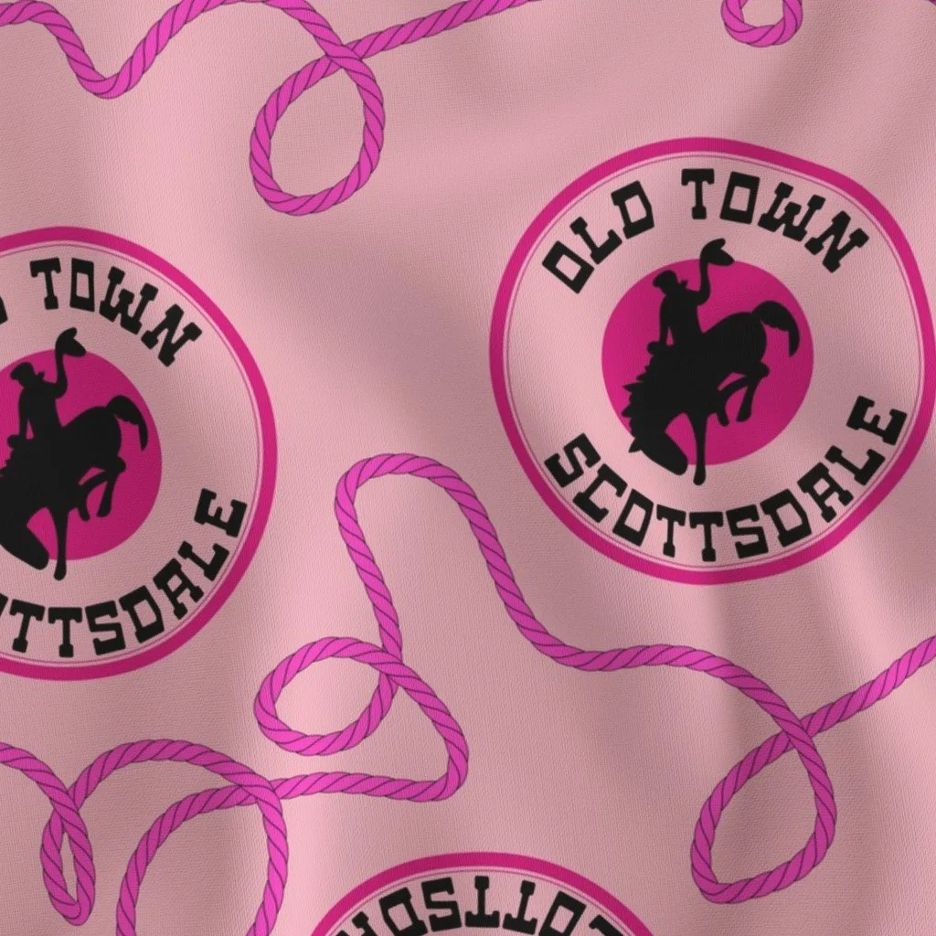 Light pink fabric printed with looping magenta lasso ropes and circular emblems depicting a cowboy silhouette on a bucking bronco with the text "OLD TOWN SCOTTSDALE."