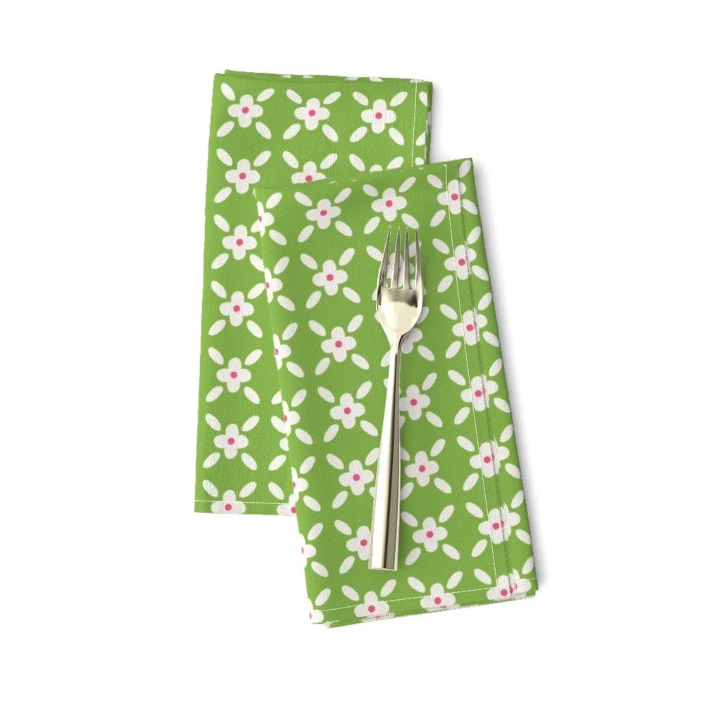 Folded apple-green cloth napkins topped with a silver fork, featuring a geometric pattern of small white flowers with pink centers.