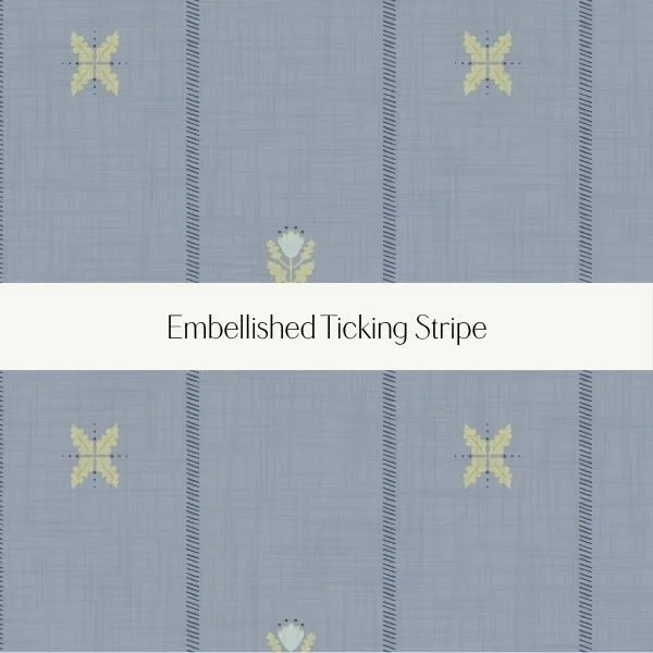 Close-up of a light blue fabric with embroidered yellow butterflies and a white strip with the text 'Embellished Ticking Stripe'.