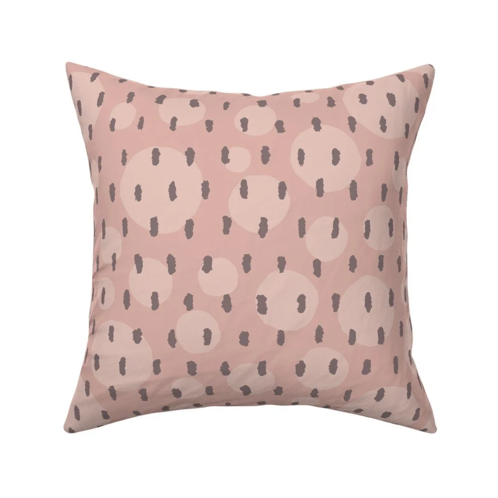 Muted dusty rose throw pillow patterned with soft circular spots overlaid with vertical dashed charcoal brushstrokes.