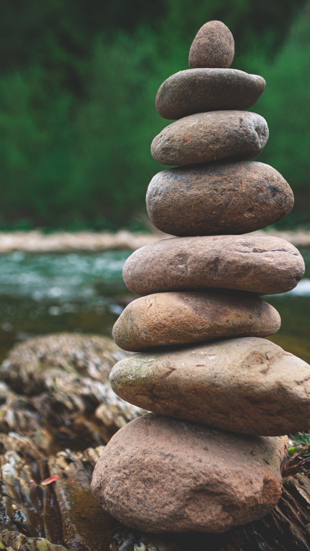 Stacked rocks on a stream in a natural setting with green foliage in the background.