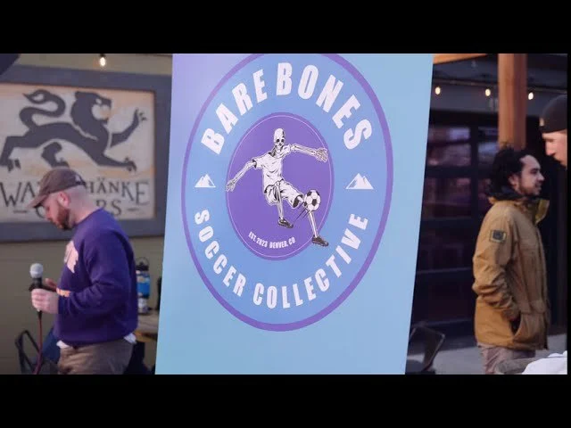 A large circular banner with the logo of Barebones Soccer Collective, featuring a skeleton playing soccer. People are gathered around at an indoor or outdoor event.