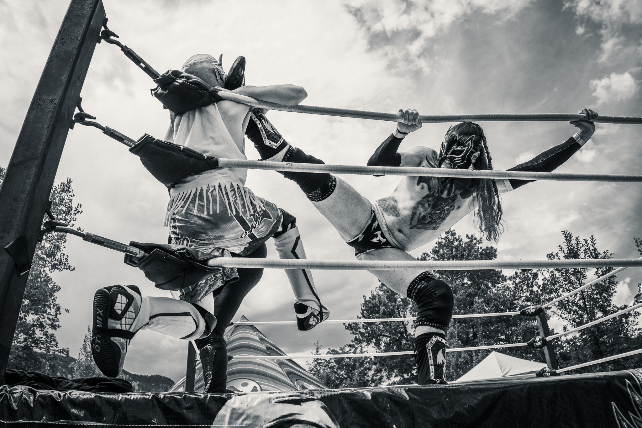 Black and white photo of two luchadores wrestling on a ring with a cloudy sky above.