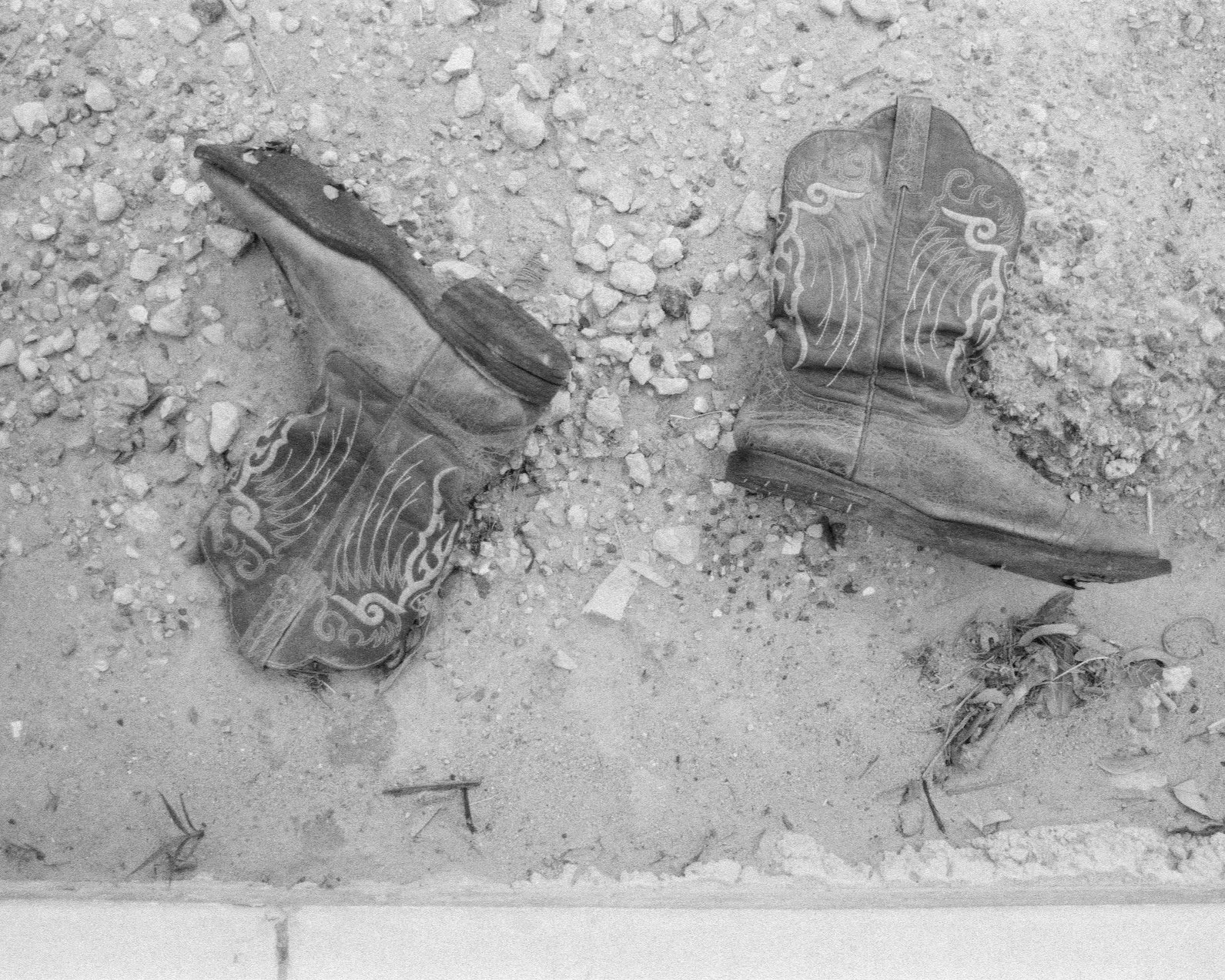 A pair of worn hiking boots on rocky ground with some debris nearby.