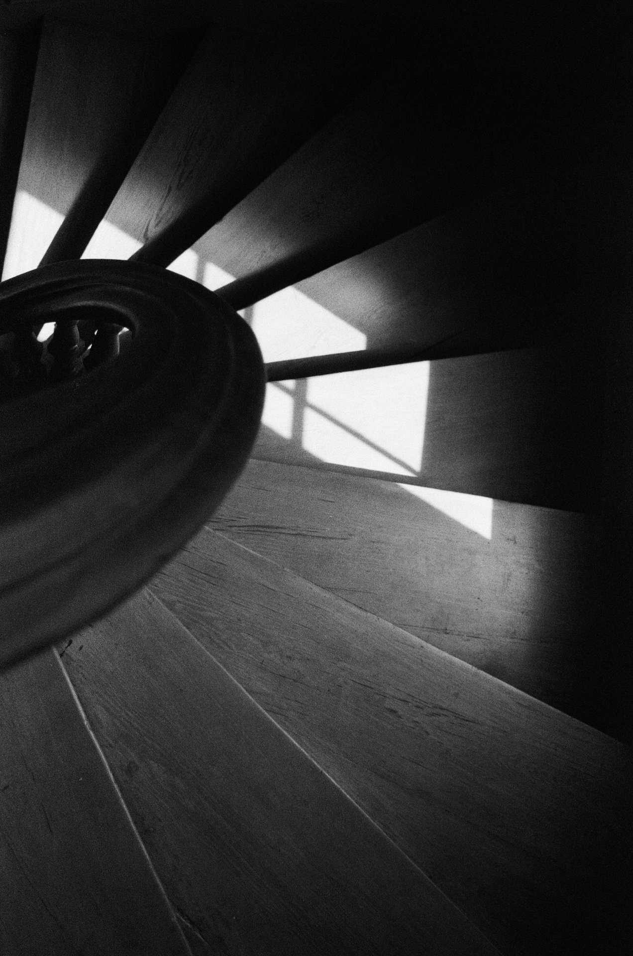 Black and white photo of a wooden staircase with a rounded handrail, casting shadows on the steps.
