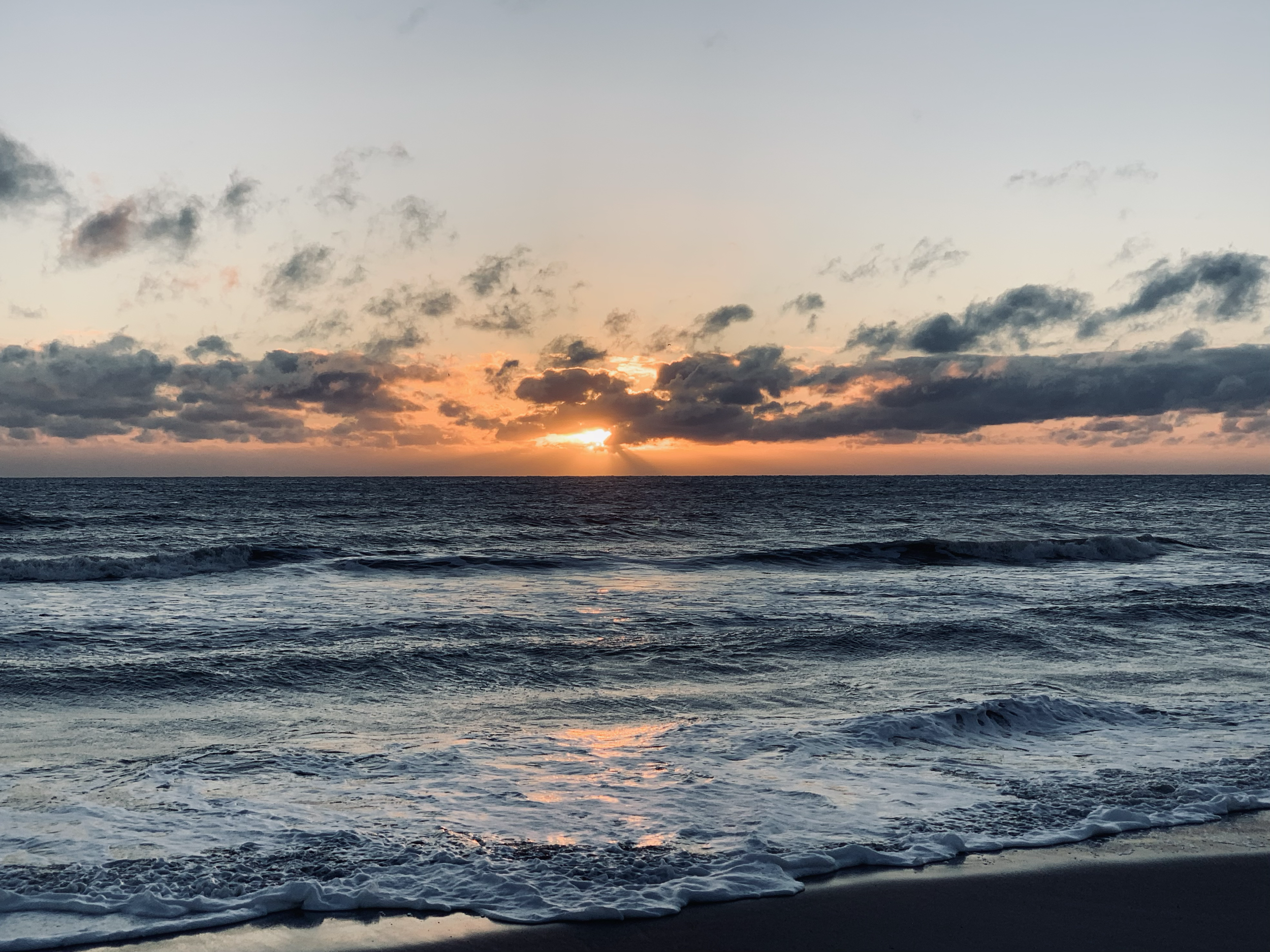 Ocean waves at sunset with a mostly clear sky and some clouds.