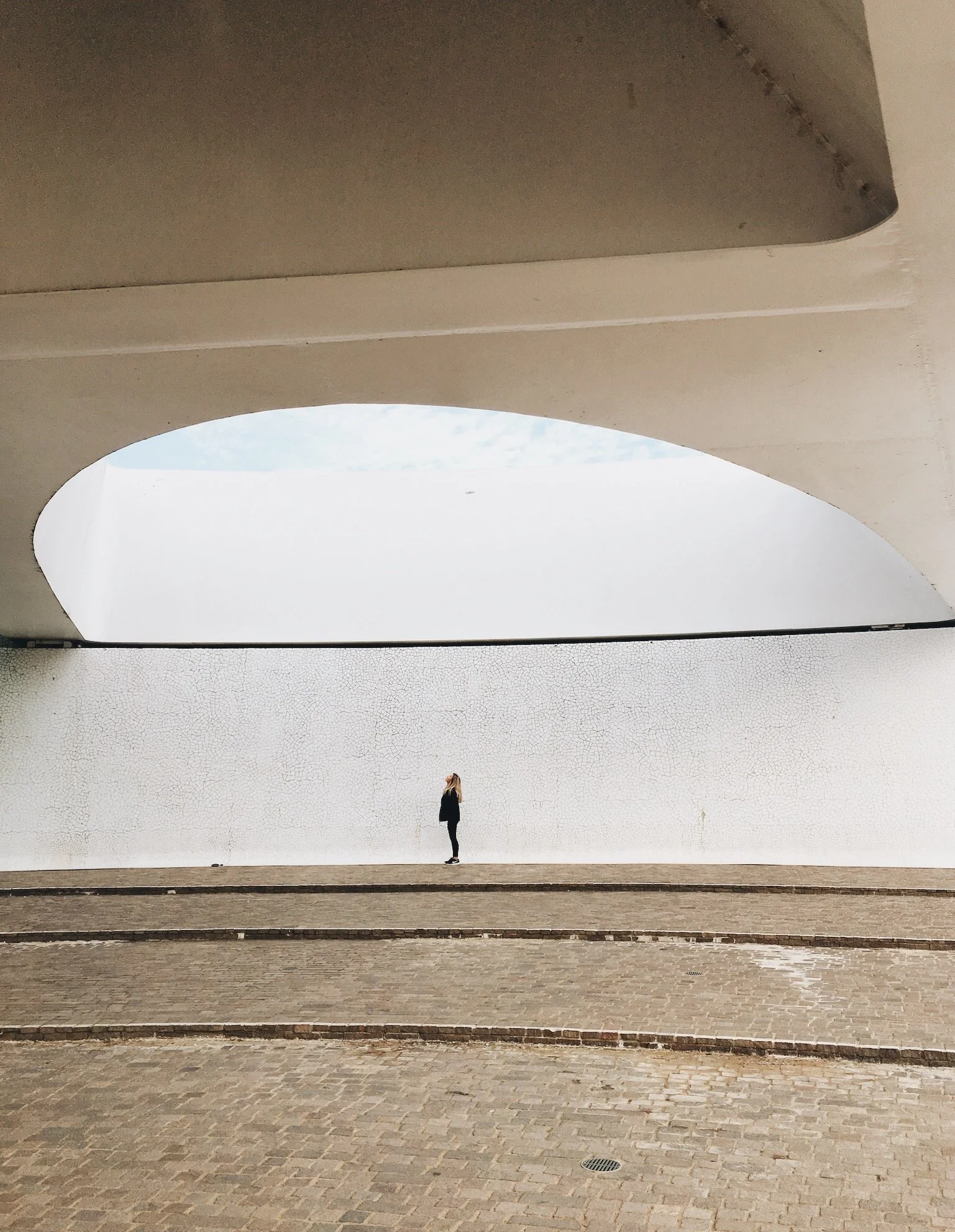 A person standing under a large, white, curved architectural structure with a sky visible through an opening above.