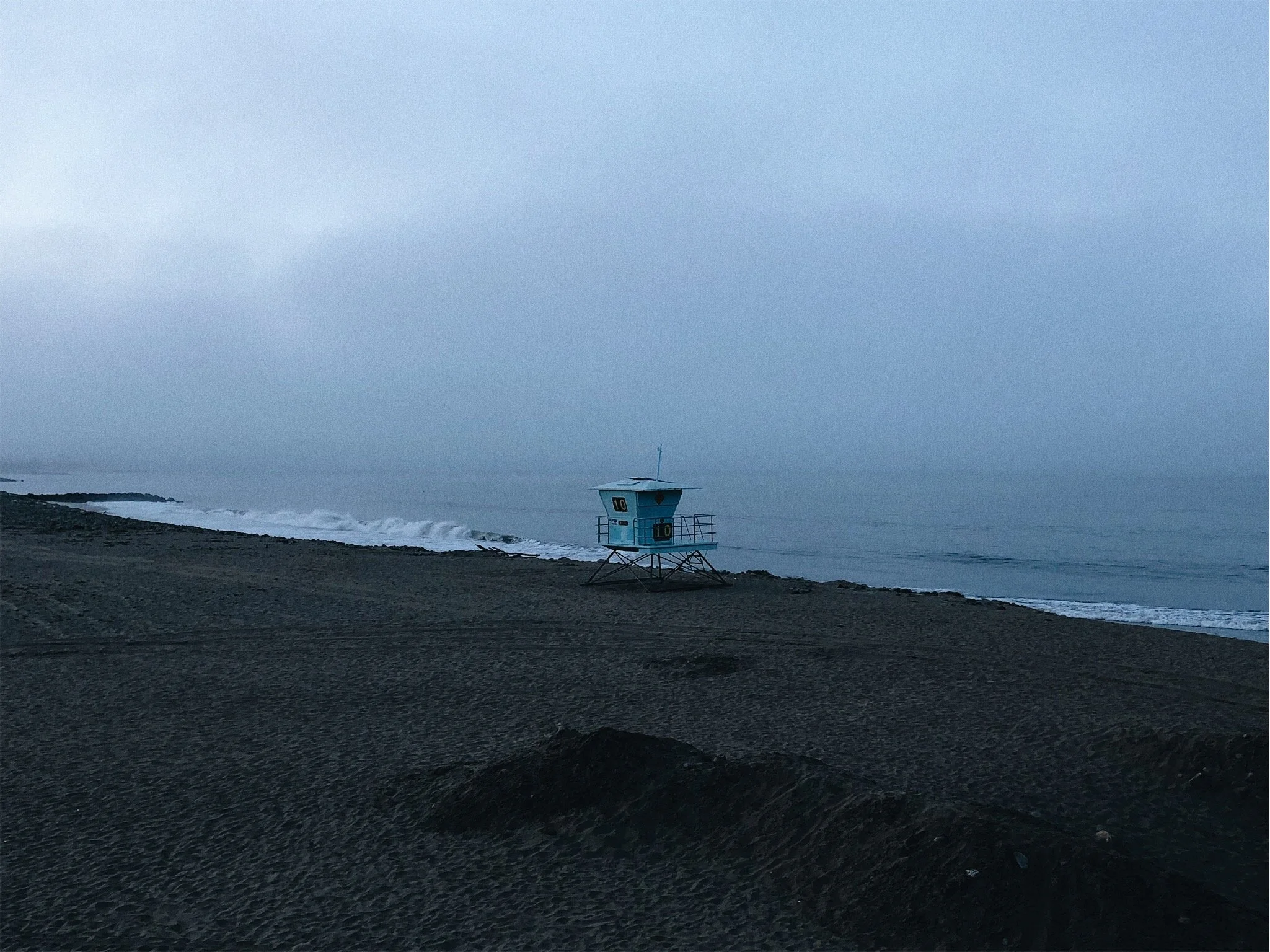 A lifeguard tower on a beach during dusk or early morning with calm ocean waves in the background.