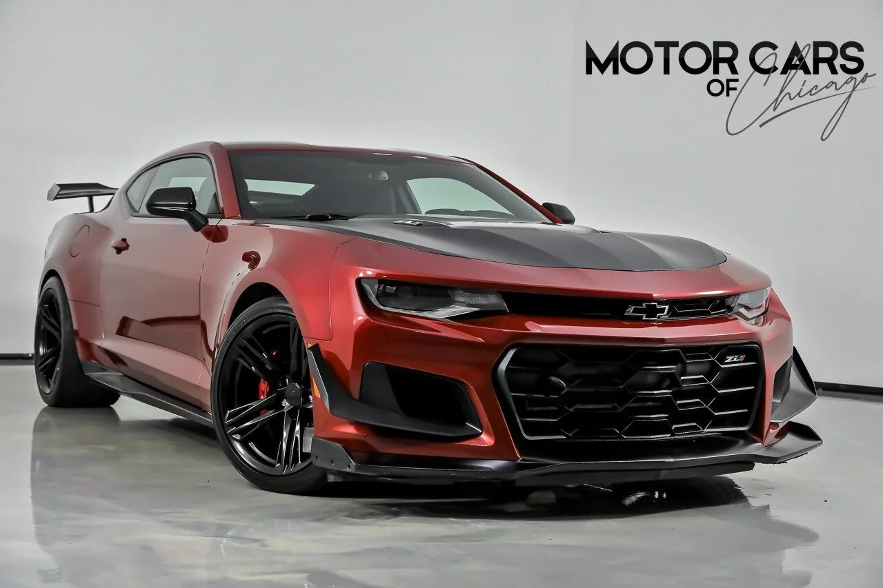 Red and black Chevrolet Camaro race car with black wheels, spoiler, and aggressive front grille, displayed indoors at Motor Cars of Chicago.