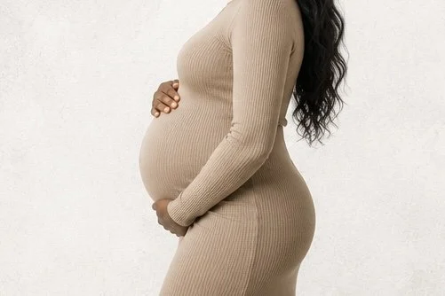 Side view of a pregnant woman wearing a beige, long-sleeve, ribbed dress, cradling her belly.