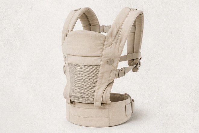 Beige baby carrier with shoulder straps and mesh front pocket on a plain background.