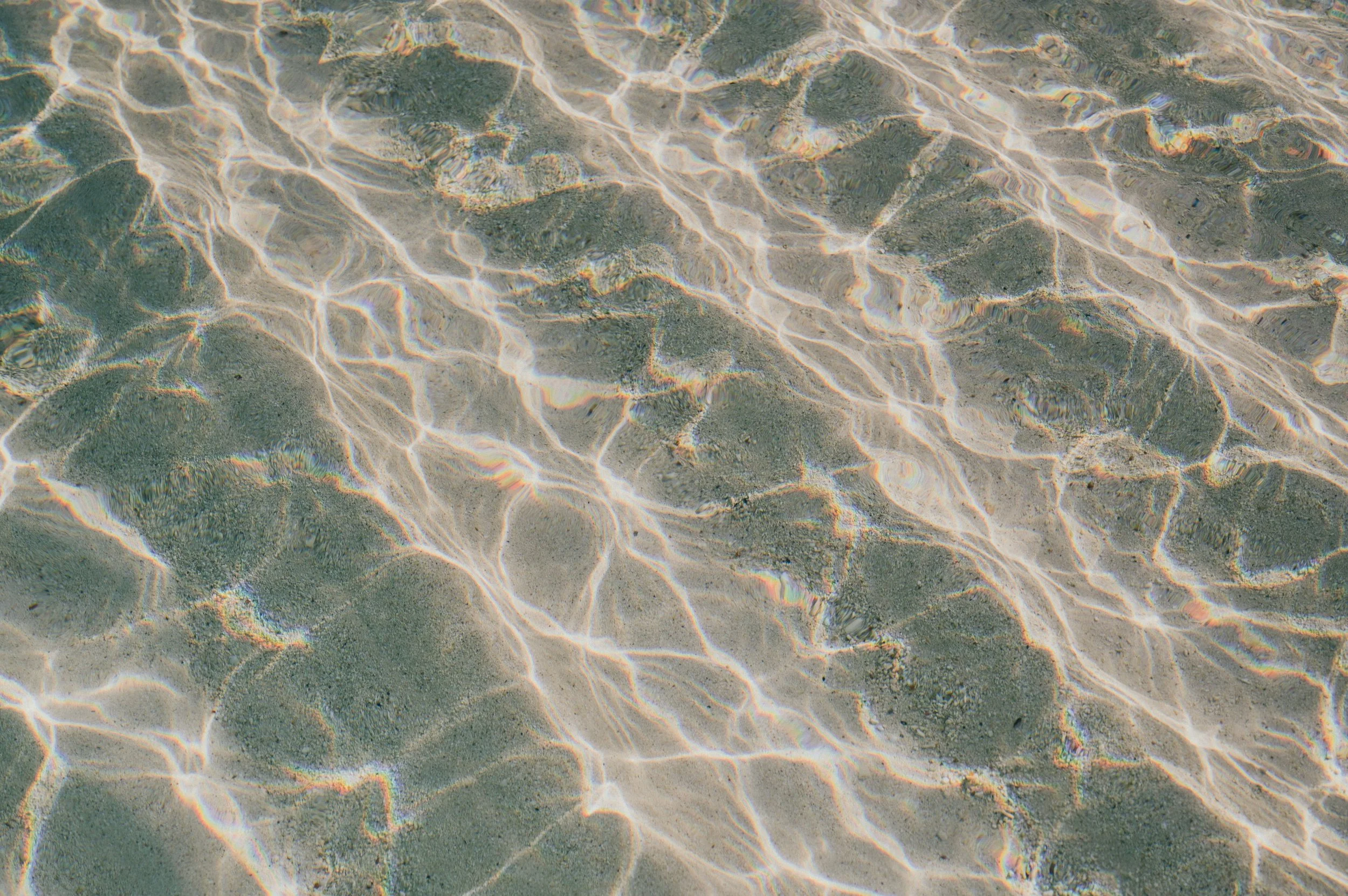 Clear water revealing sandy and rocky bottom with light reflections.