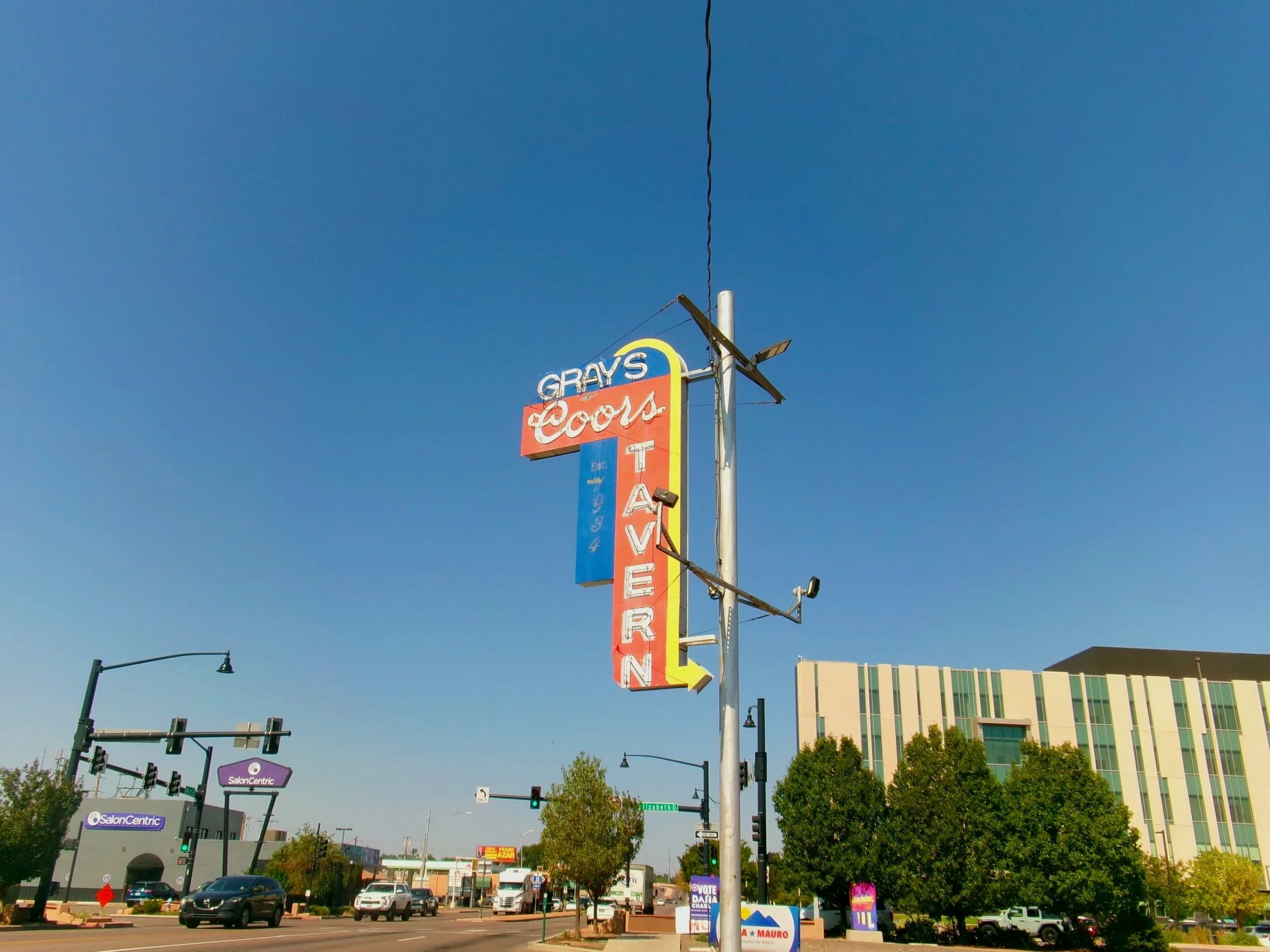 A tall signboad for a casino with the words 'GRAYS', 'COORS', and 'TAVERN' visible against a clear blue sky. The sign has a red, yellow, and blue color scheme.