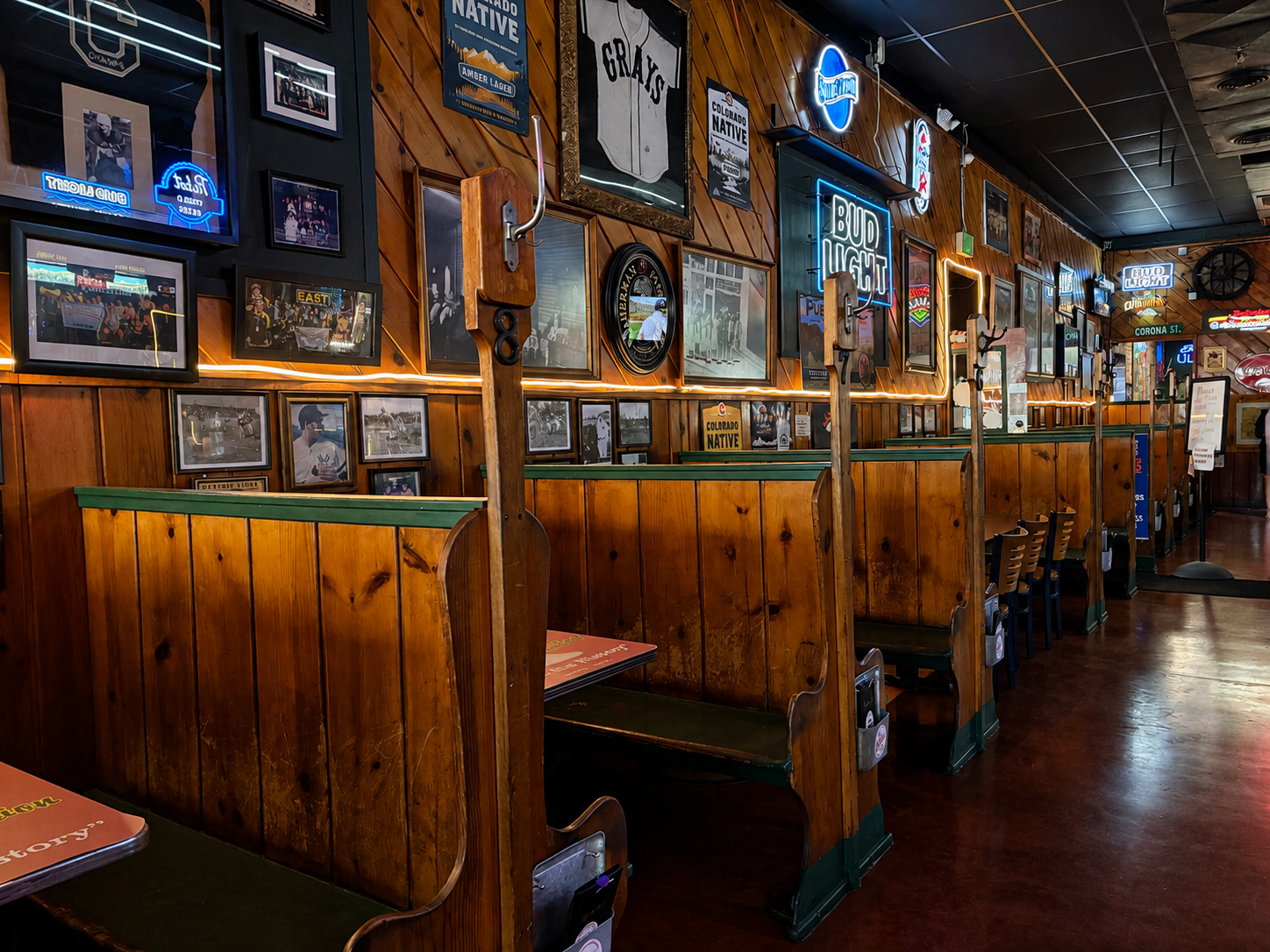 Interior of a restaurant with wooden booths, framed photos, neon signs, and various posters on the walls.