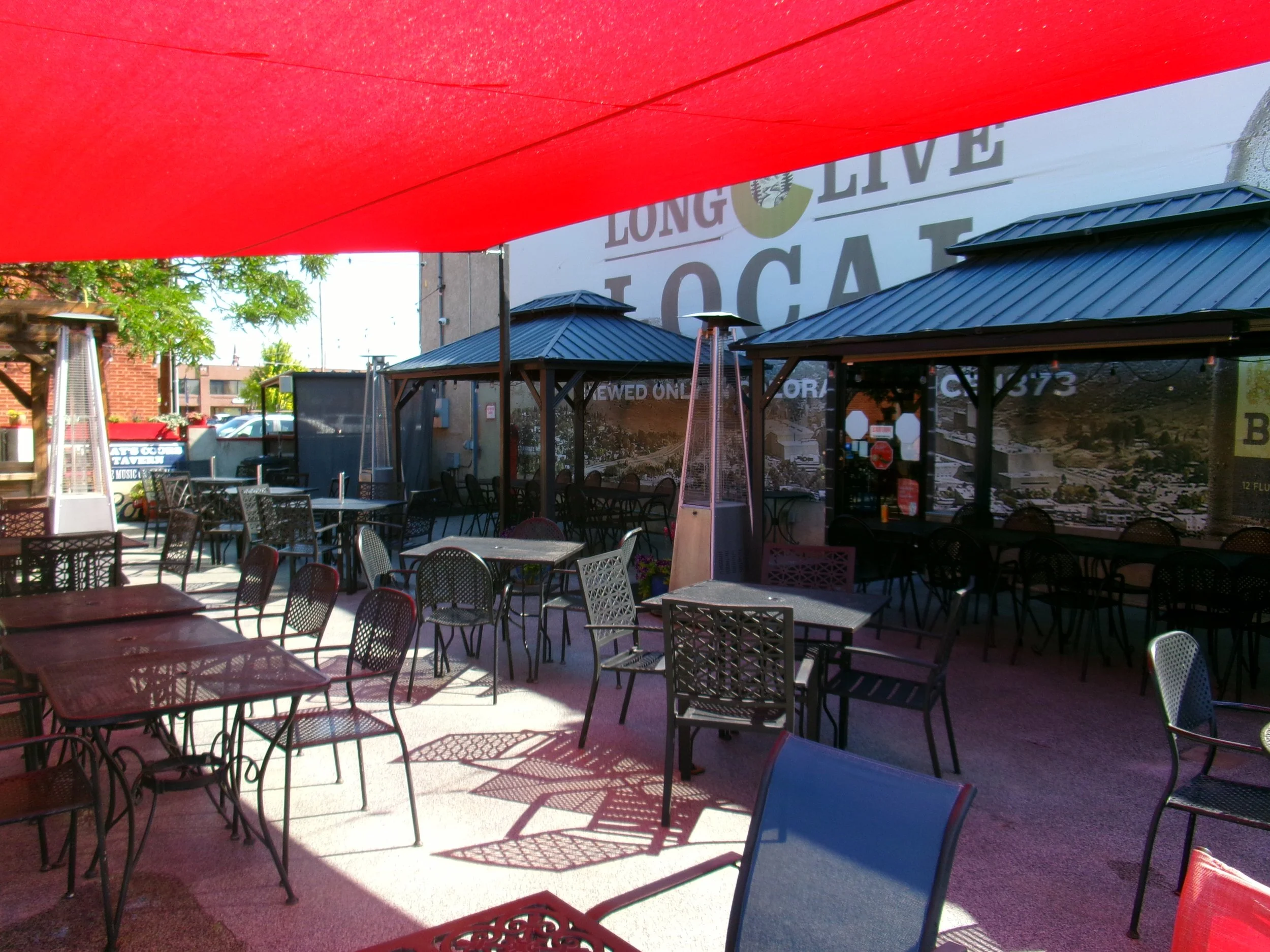 Outdoor seating area with tables and chairs shaded by a large red umbrella.