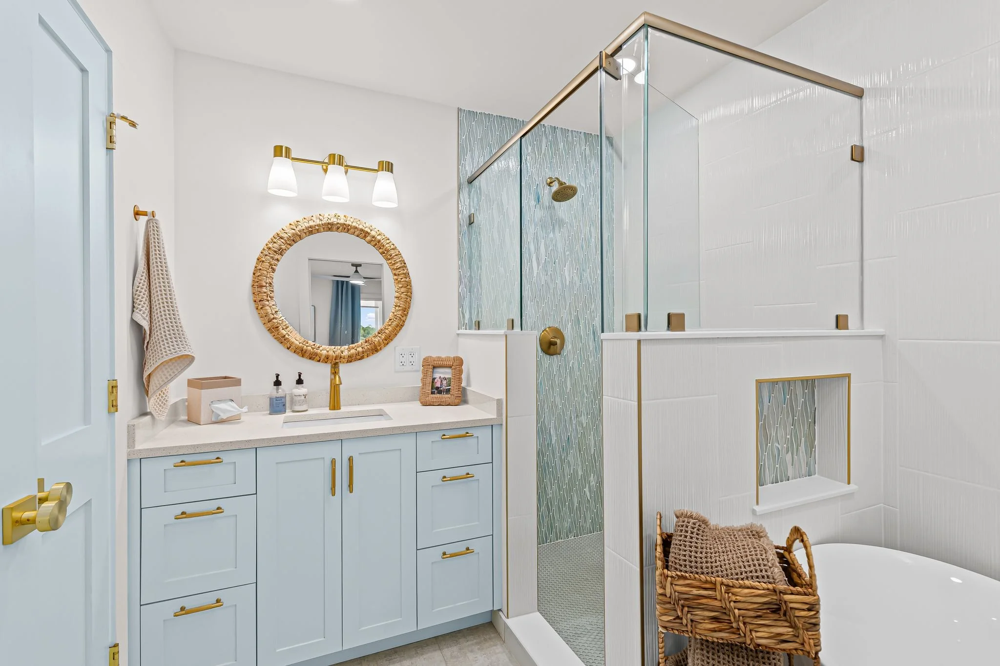Renovated bathroom with a light blue vanity, glass-enclosed shower, textured blue tile, and warm brass accents.