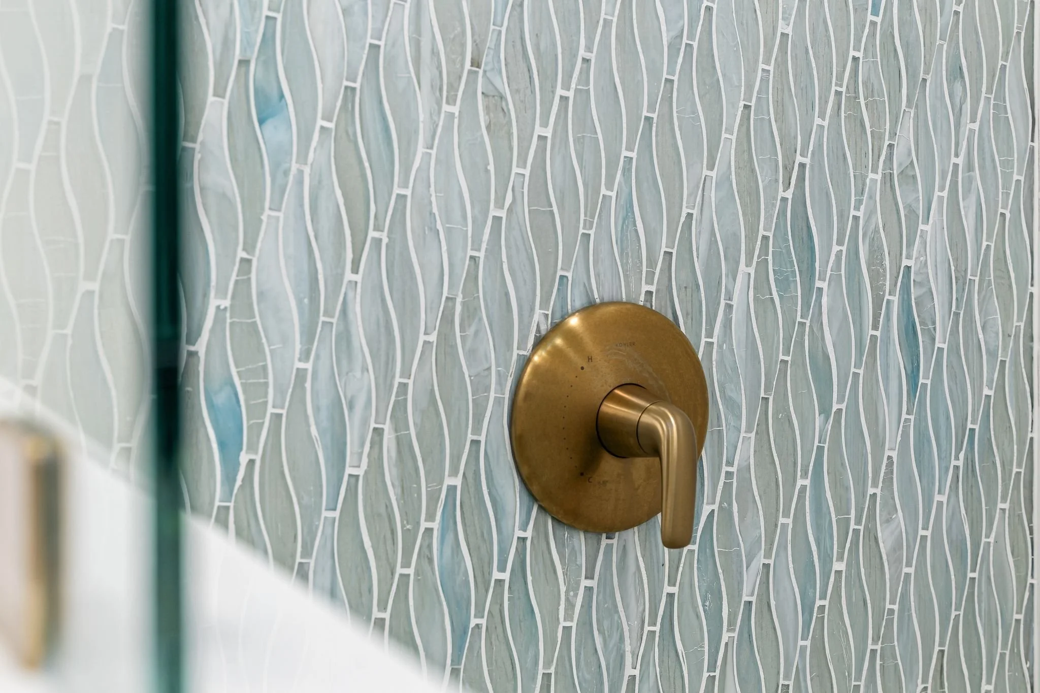 Brass shower fixture against textured blue tile in a renovated bathroom.