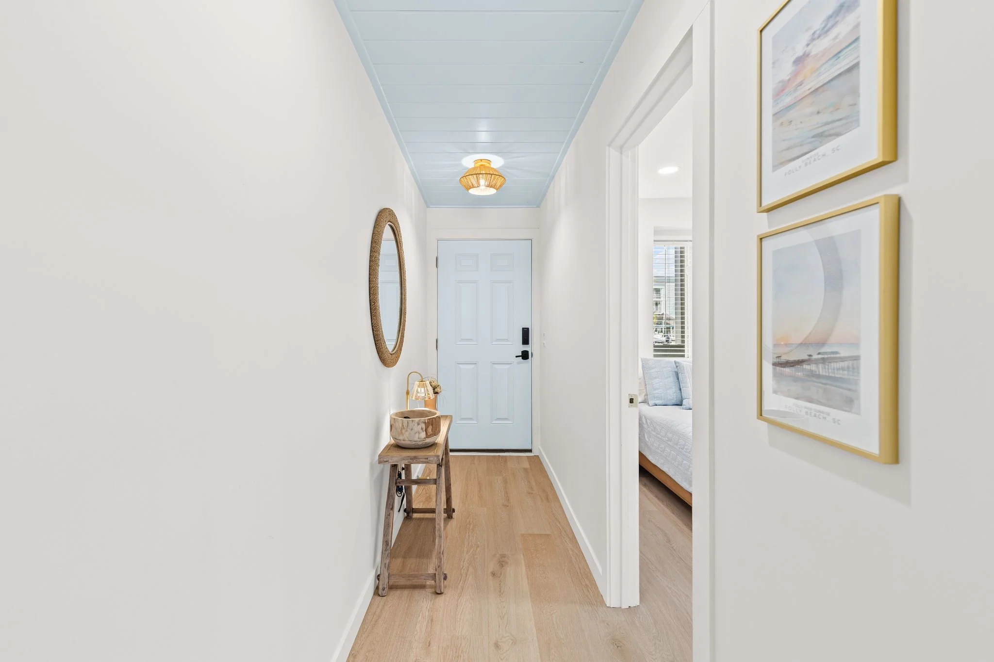 Bright hallway with light wood flooring, framed artwork, and simple coastal-inspired furnishings.
