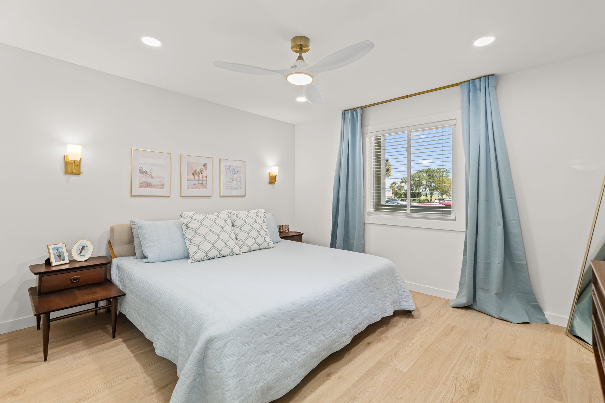 Light-filled bedroom with soft blue accents, light wood flooring, and simple furnishings.