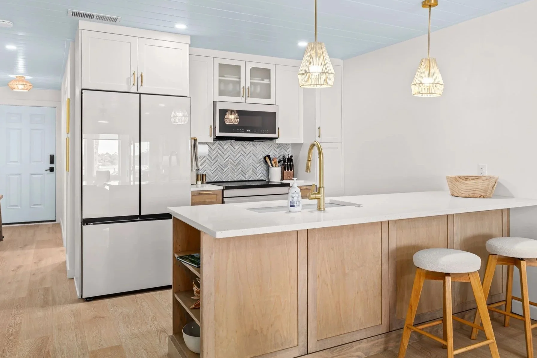 Renovated kitchen with white cabinetry, wood island, gold fixtures, and pendant lighting.