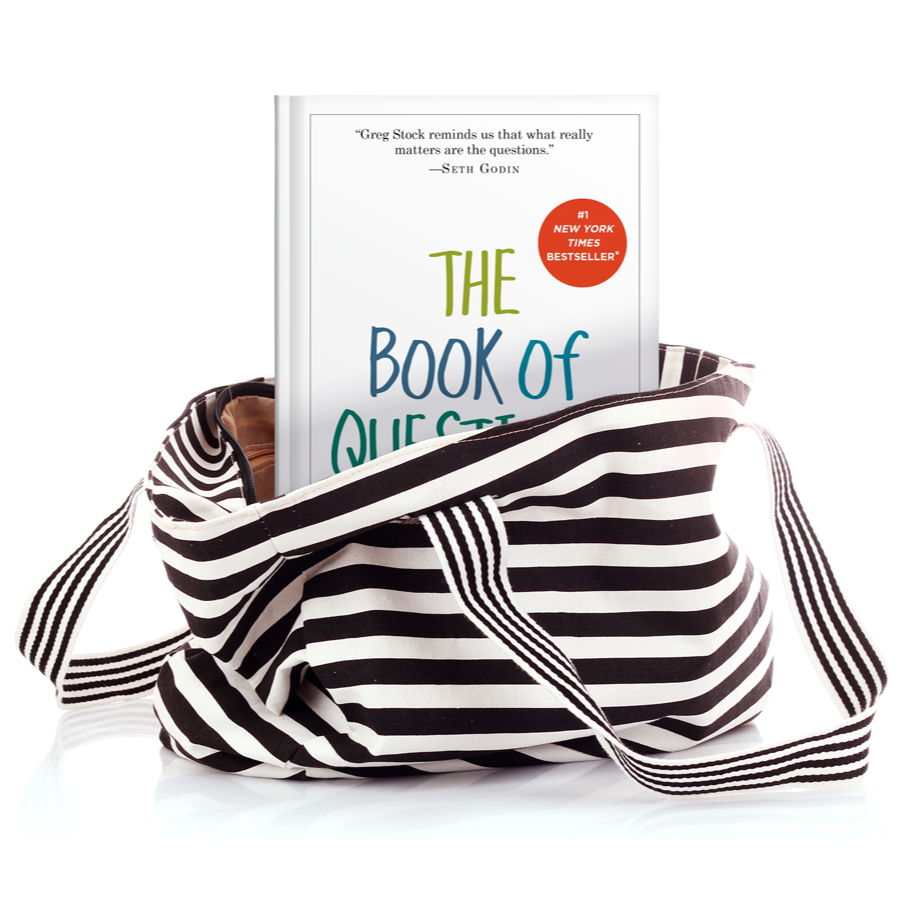 A striped black and white tote bag contains a copy of the book 'The Book of Questions' by Greg Stock, with a red sticker indicating it's a New York Times bestseller, set against a white background.