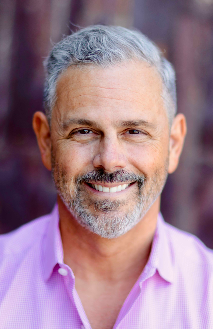Headshot of Scott SImon smiling outdoors, wearing a light purple collared shirt.