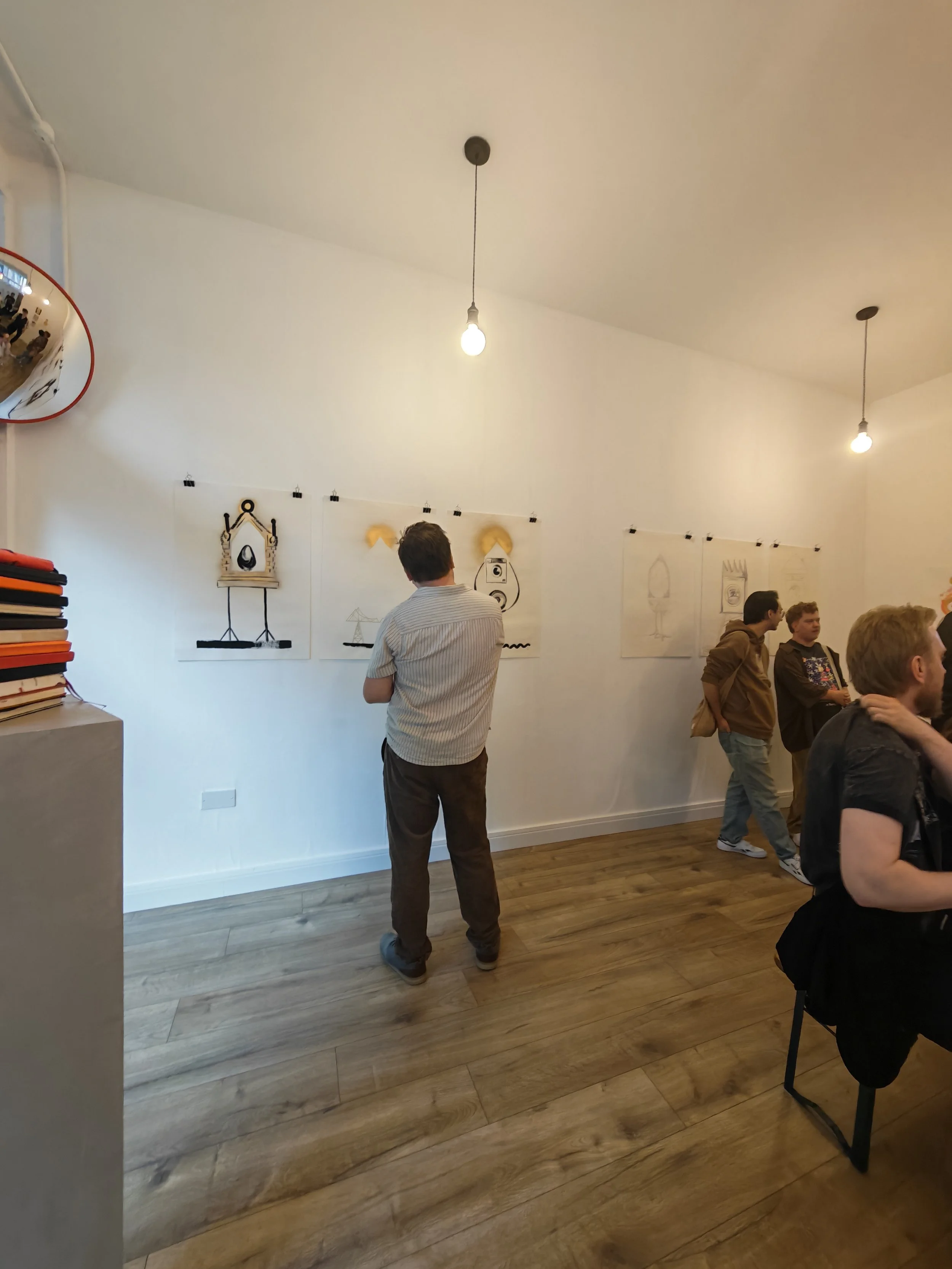 People standing and talking in an art gallery with hanging illustrations on the wall.