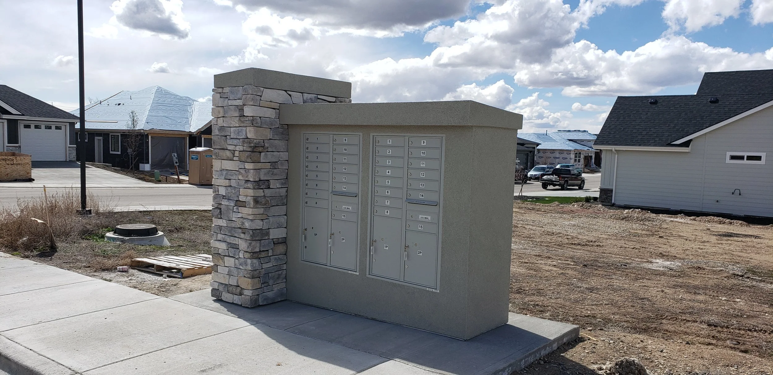 Mailboxes in a modern residential area with new construction houses and a partly cloudy sky.