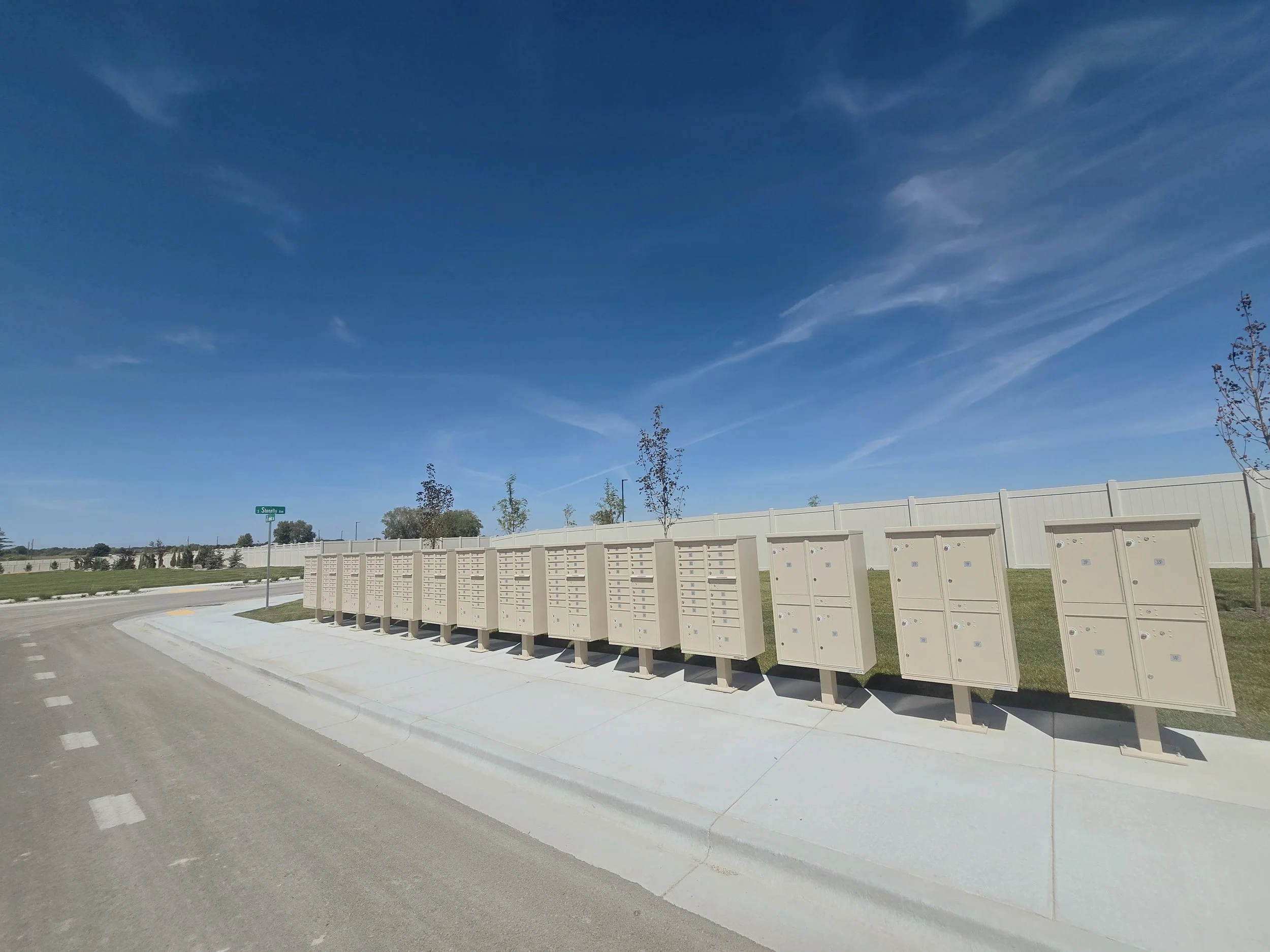 A clear day sky with wispy clouds over a row of mailboxes and a green street sign reading 'Stonely Ave' in a suburban area.