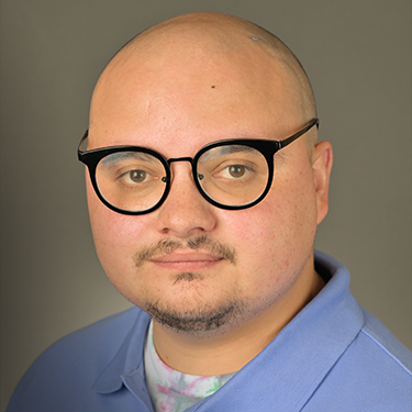 A bald mans face with thick black glasses